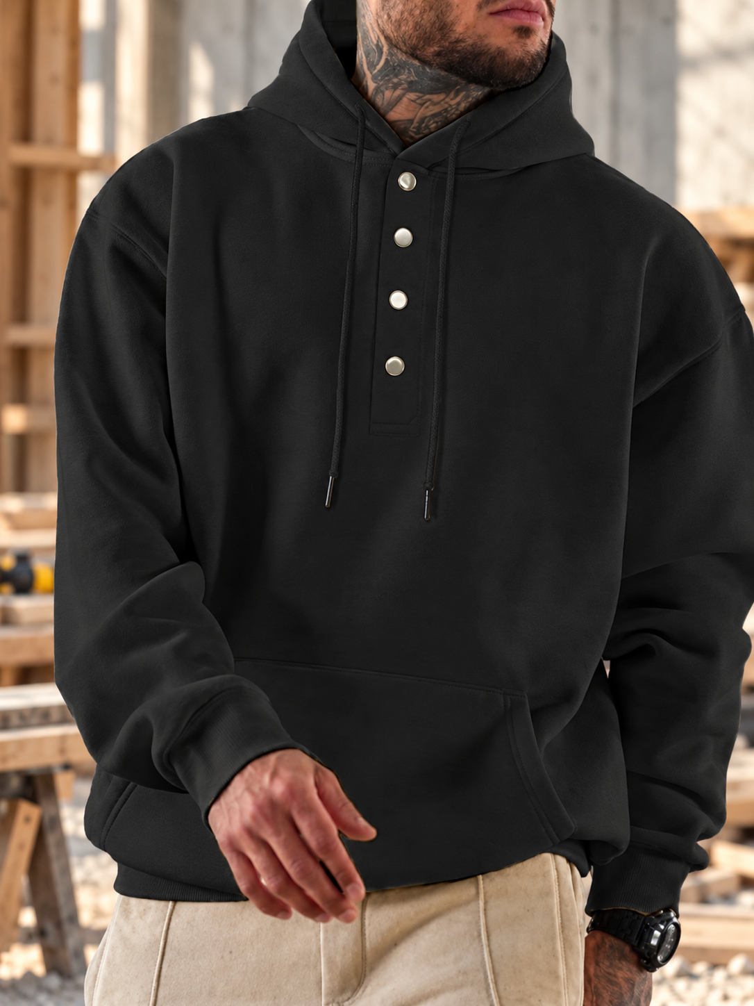 Model wearing a black four-button drawstring hoodie in a rugged workshop